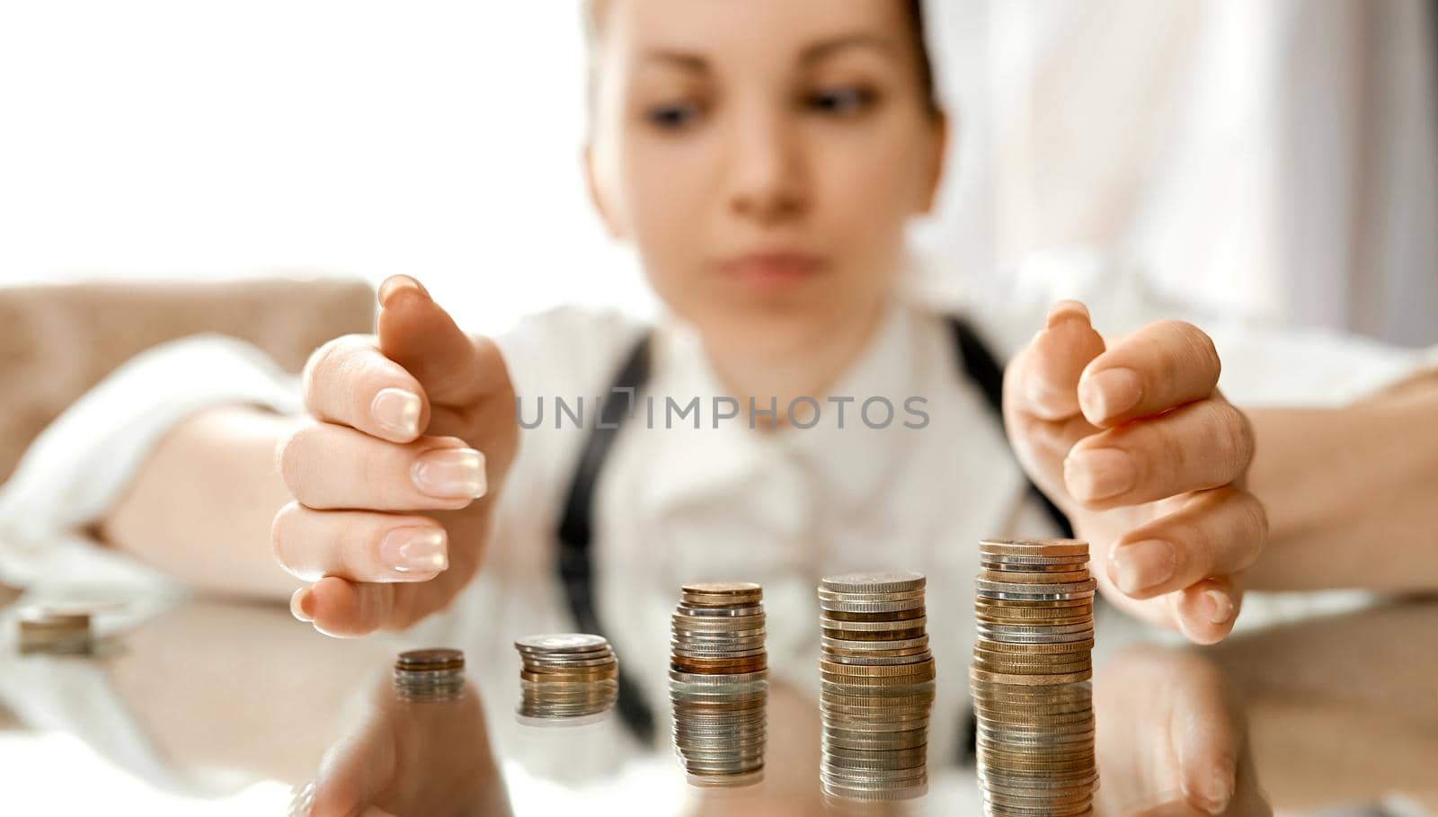 A woman collects stacks of coins to the center on a mirrored table . High quality photo