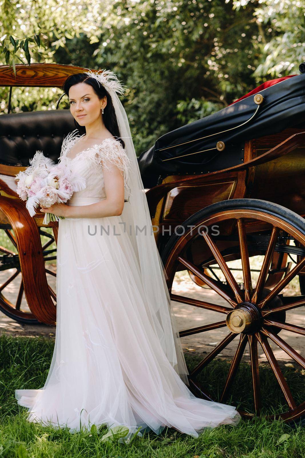 A stylish bride with a bouquet stands near a carriage in nature in retro style.