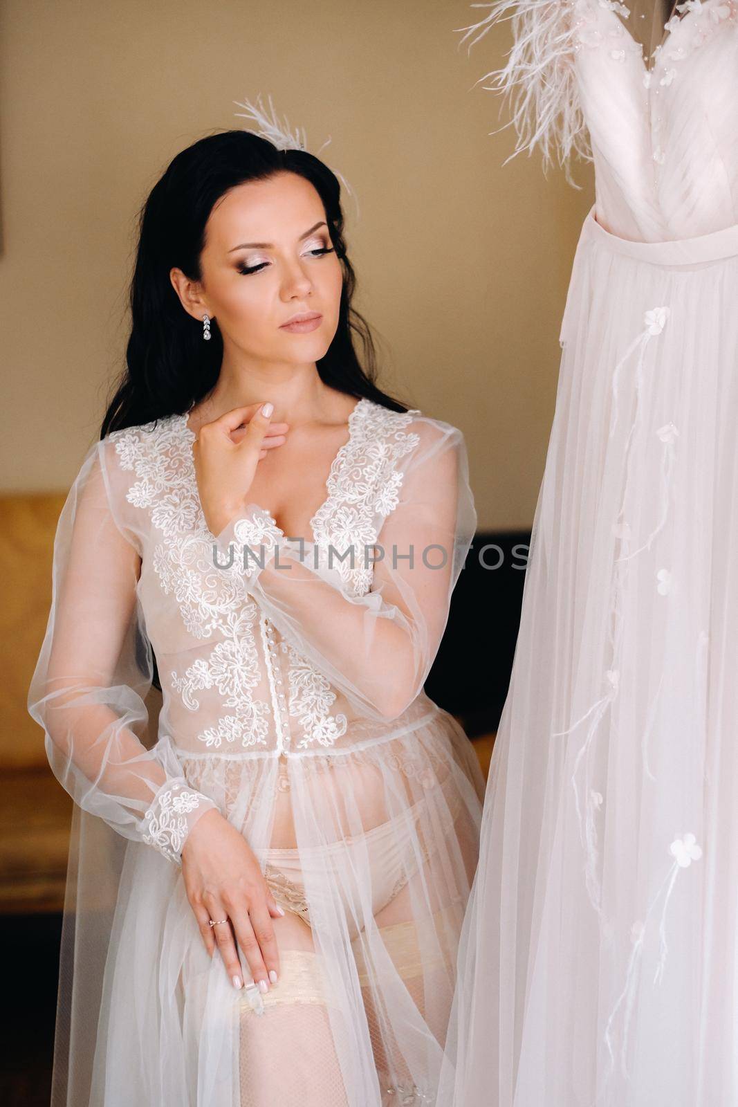 the bride, dressed in a boudoir transparent dress and underwear, stands at home in the morning.