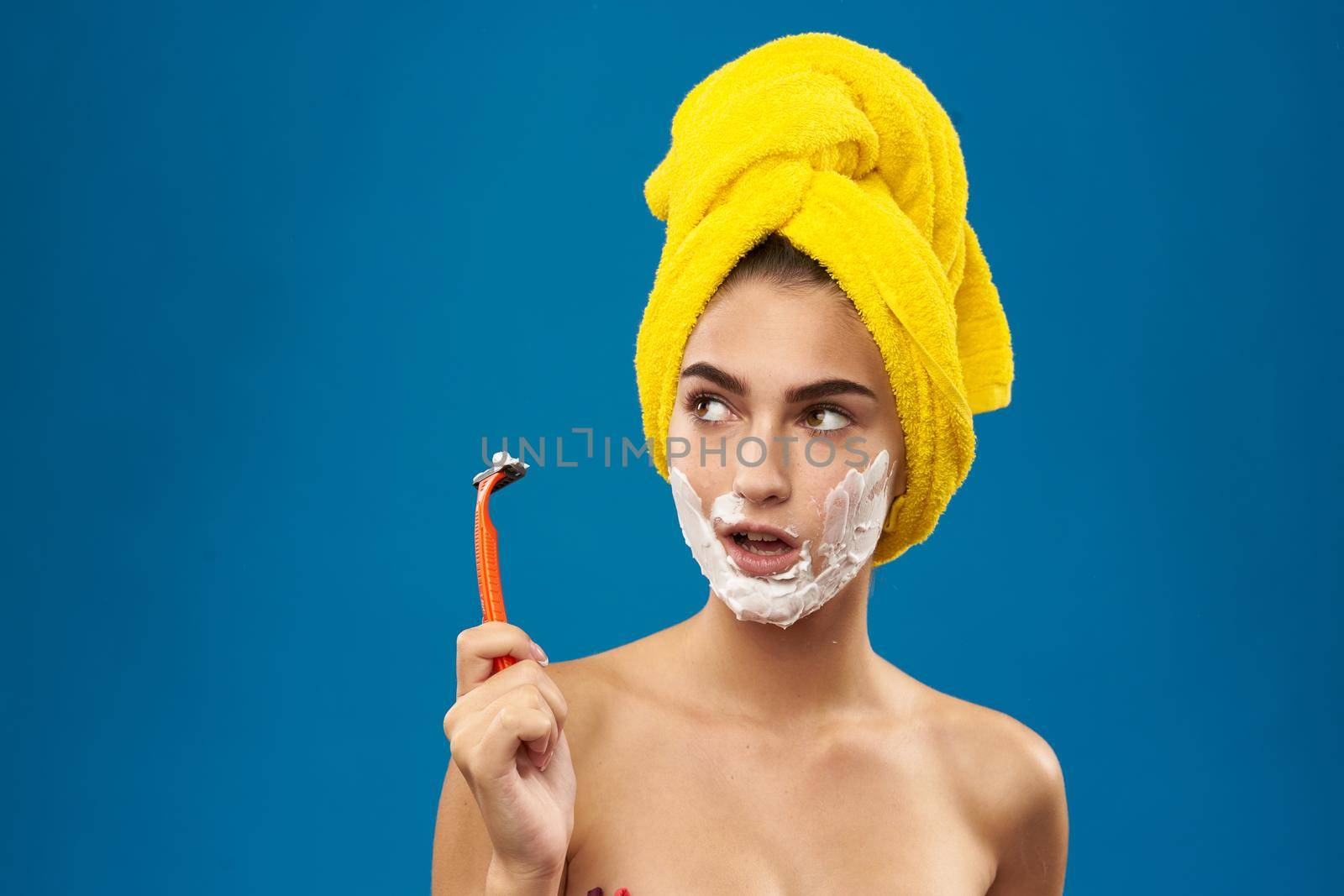 cheerful woman with a yellow towel on his head shaving blue background. High quality photo