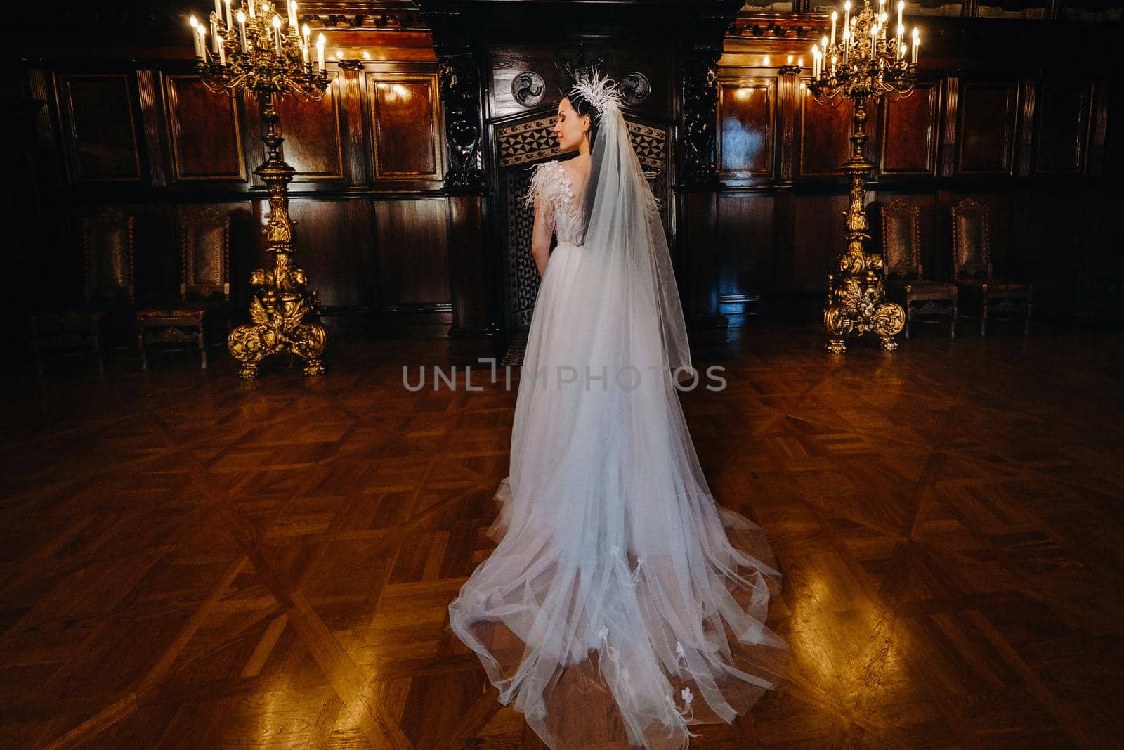 A bride in a wedding dress stands with her back in the ancient interior of the castle.