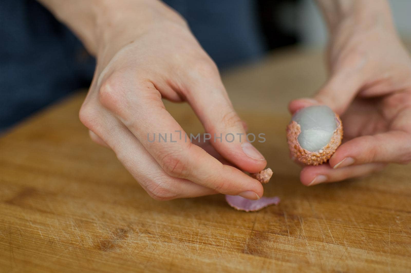 Female hands hold a litchi fruit, lychee on a wooden desk. Exotic fruits, healthy eating concept.