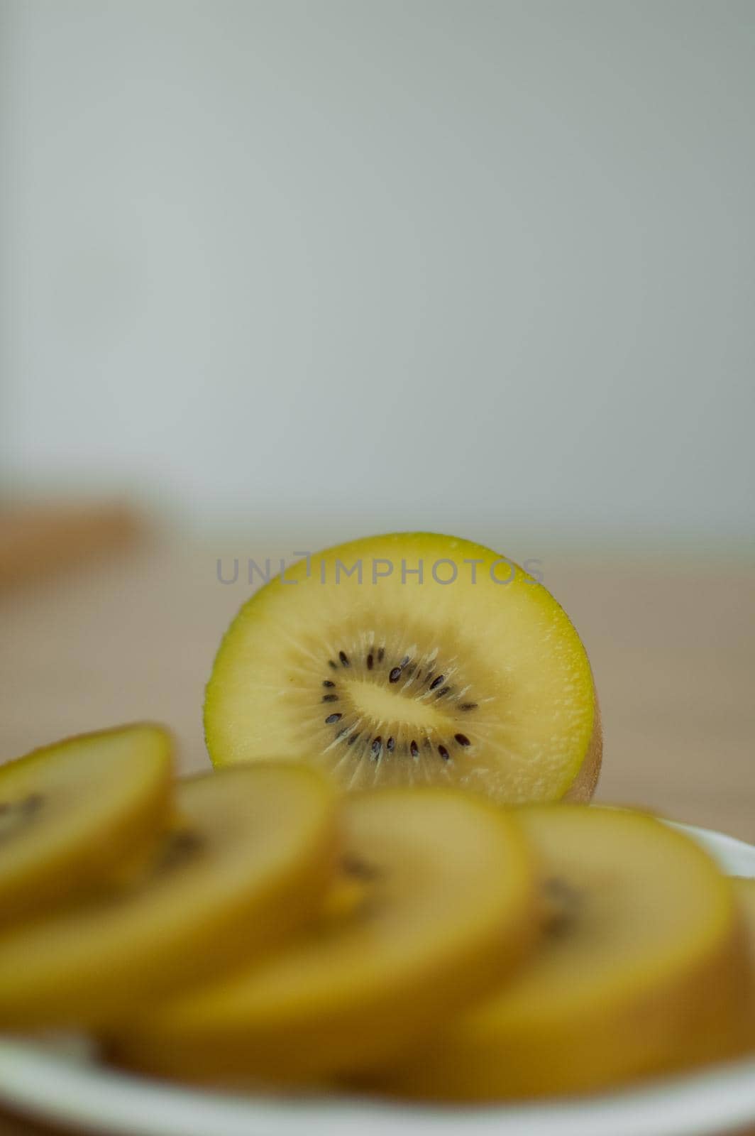 Slices of golden kiwi with yellow pulp on white plate on the kitchen. Exotic fruits, healthy eating concept by balinska_lv