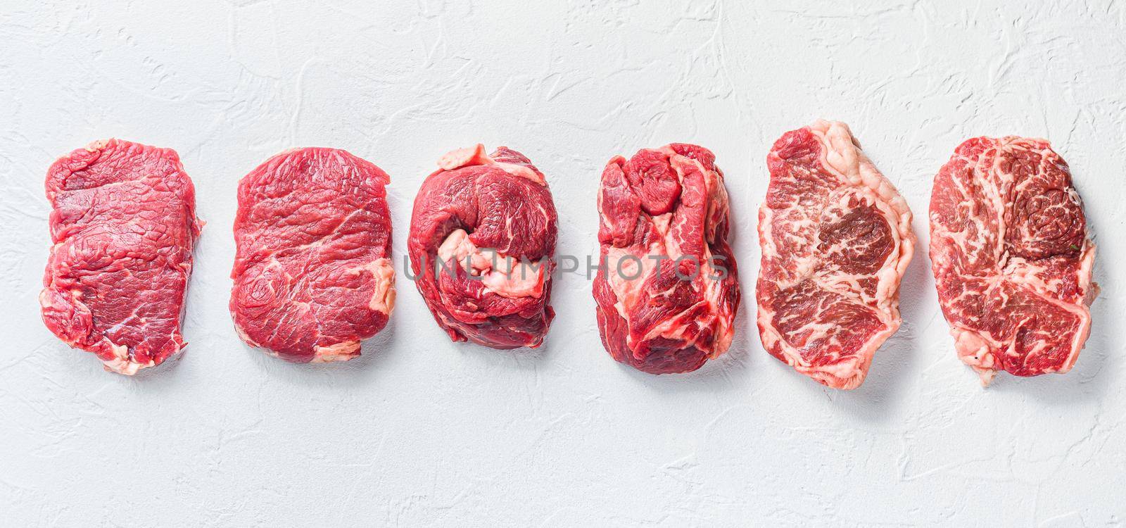 A set of different types of raw beef steaks:top blade, rump, chuck eye roll over white concrete background top view big size pano. by Ilianesolenyi