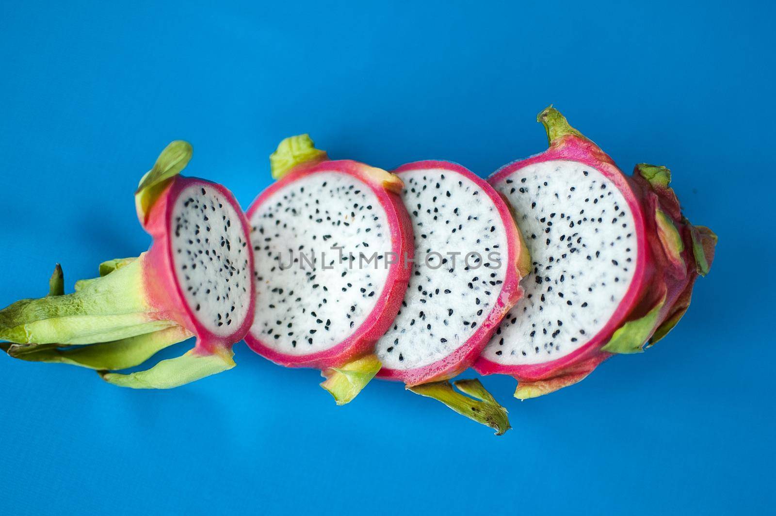 Slices of dragon fruit or pitaya with pink skin and white pulp with black seeds on blue background. Exotic fruits, healthy eating concept.