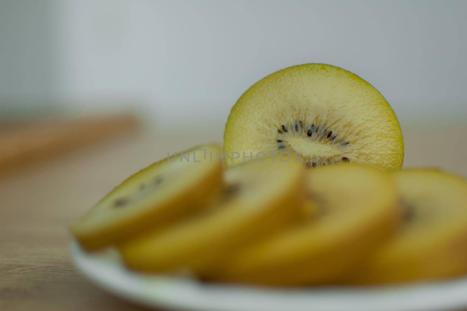 Slices of golden kiwi with yellow pulp on white plate on the kitchen. Exotic fruits, healthy eating concept.