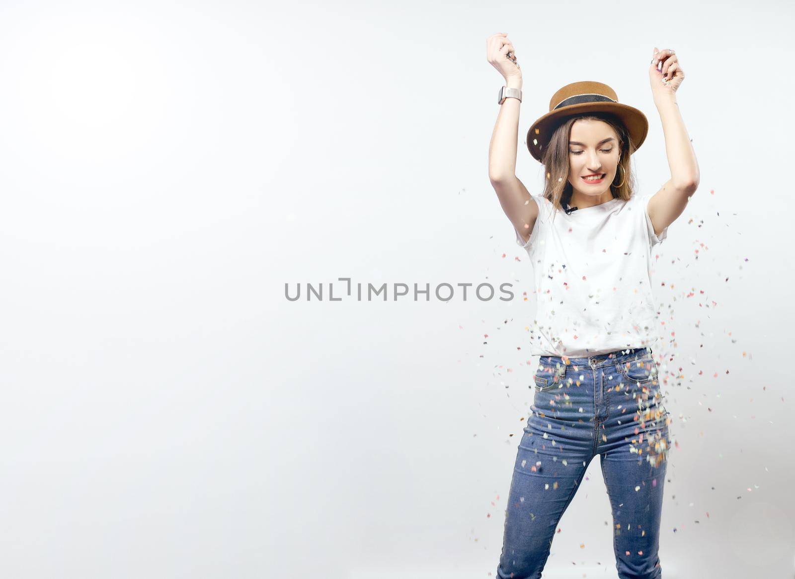 Portrait of a cheerful beautiful girl wearing hat standing under confetti rain and celebrating isolated over white background hight quality