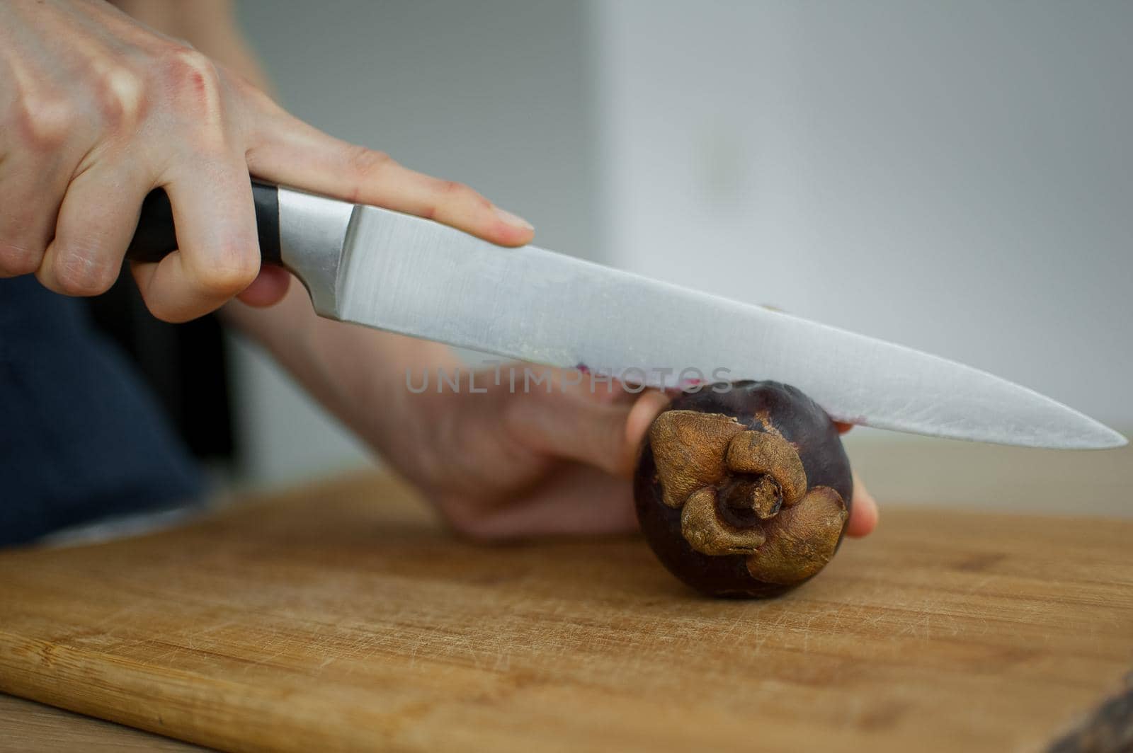 Female hands is cutting with knife a fresh ripe mangosteen on a cut wooden board. Exotic fruits, healthy eating concept.
