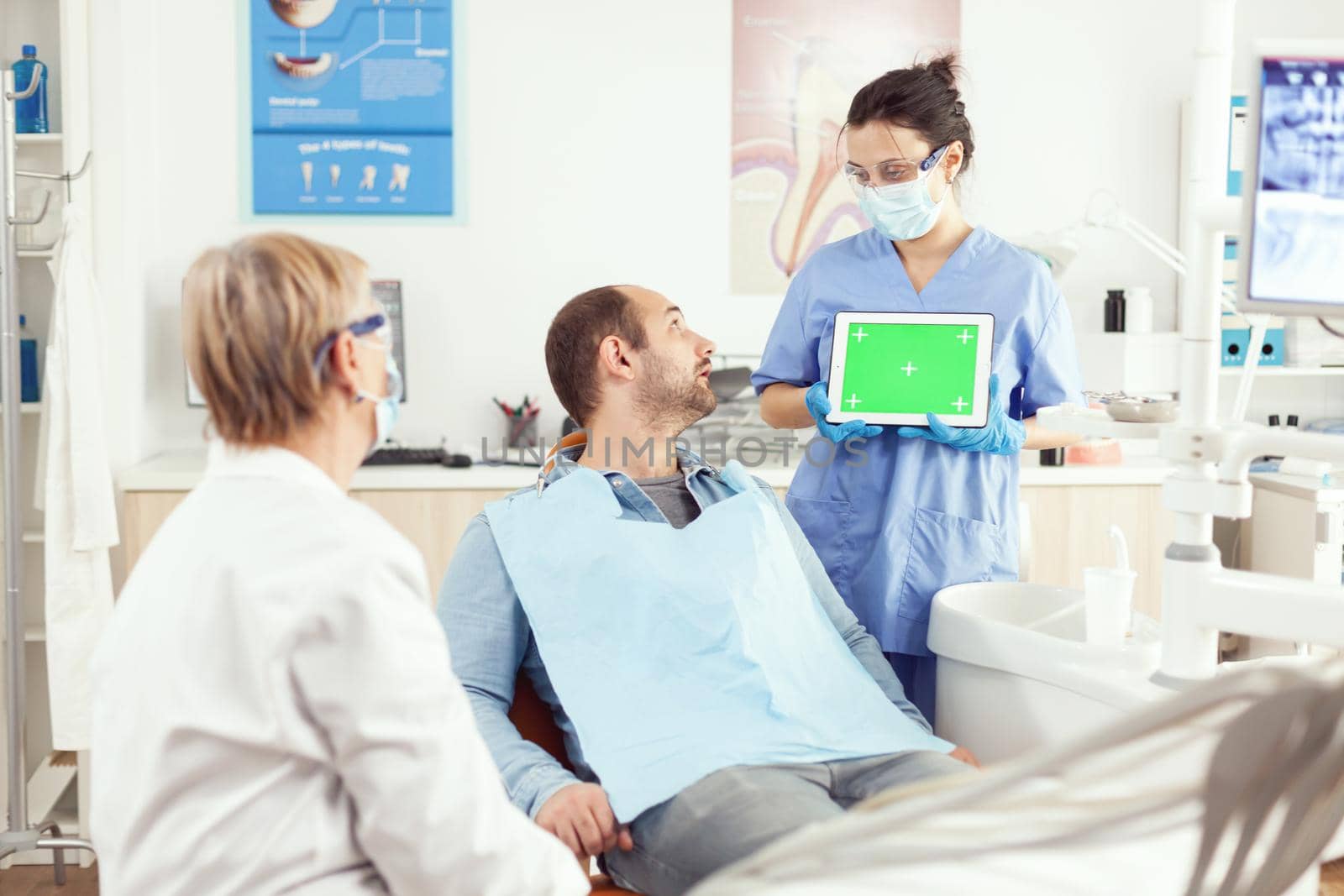 Sick patient looking at touchscreen gadget while speaking with stomatology senior doctor. Medical nurse explaining using with mock up green screen chroma key digital tablet with isolated display