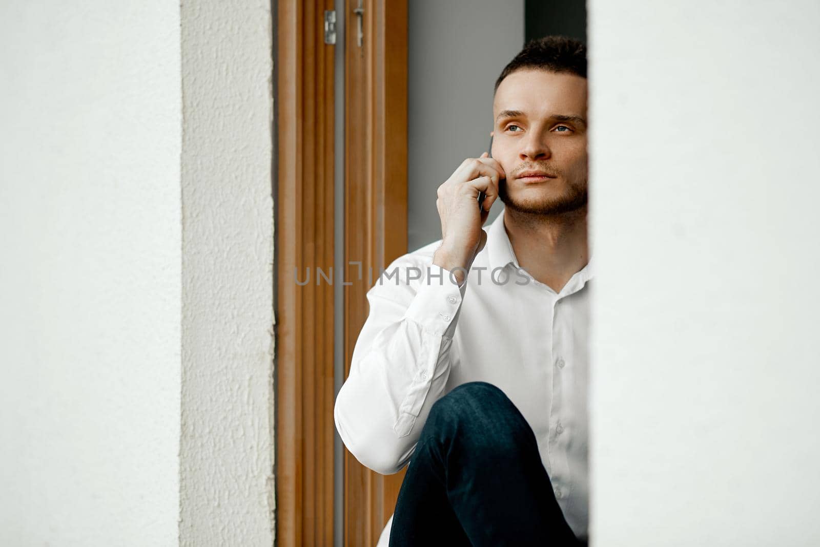 A man sits on an open window, looks at the street and talks on the phone. High quality photo