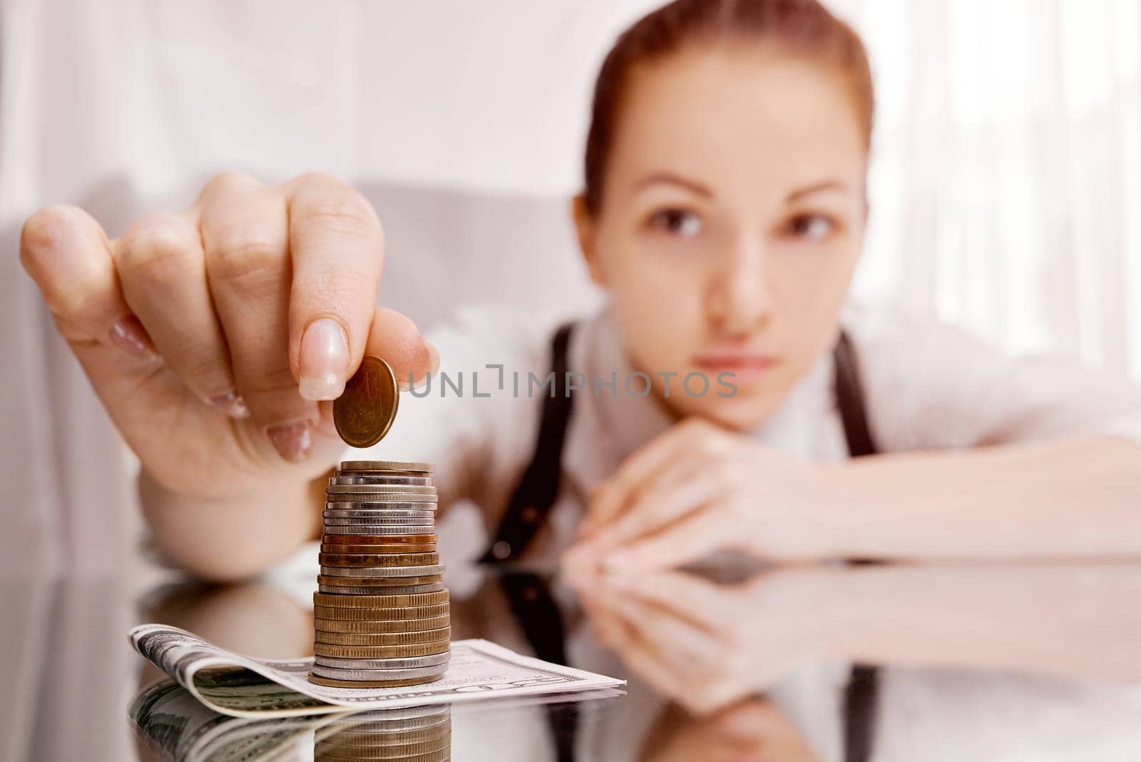 A woman puts coins in a stack on a banknote on the table. He's raising money. It's capital. by AntonIlchanka