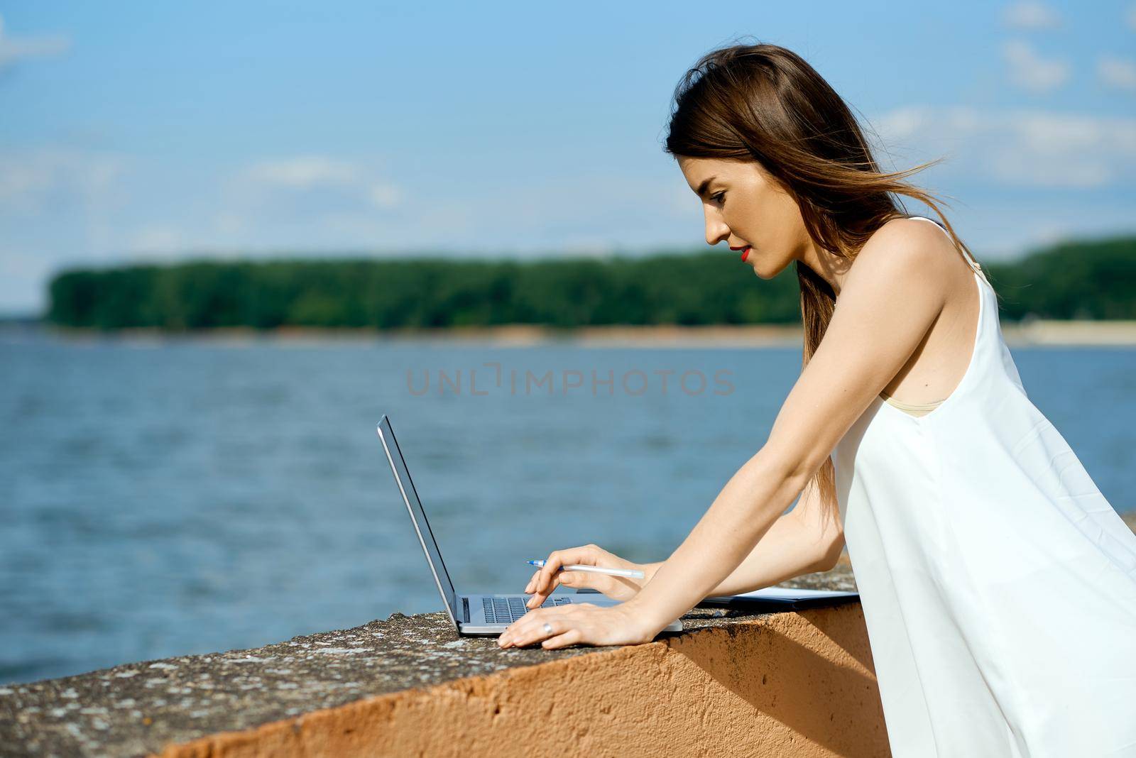 beautiful, serious girl in a white dress with a tablet, pen, laptop phone on the dock. High quality photo