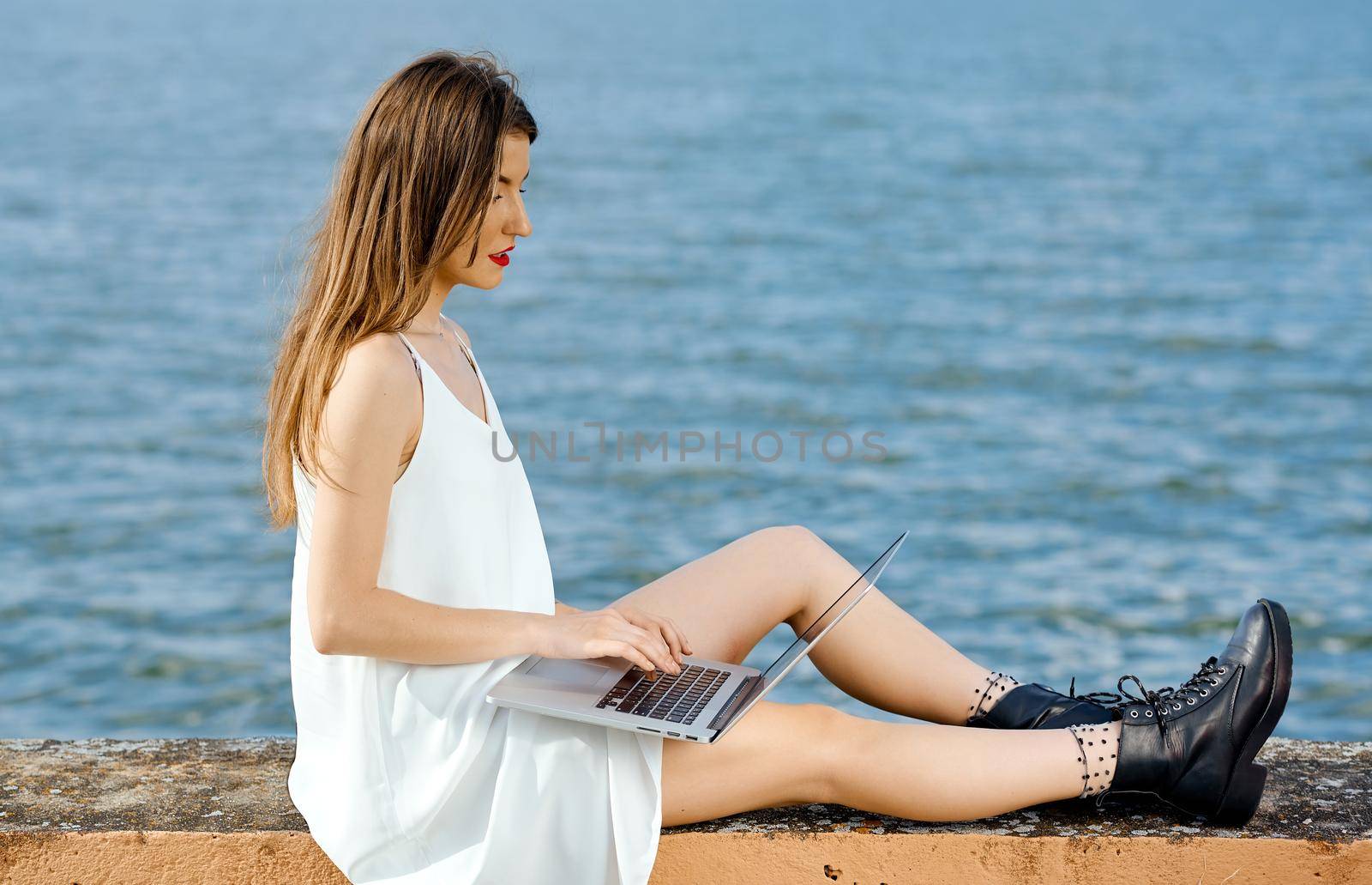 Businesswoman comfortably positioned on a concrete fence berth works behind a laptop . High quality photo