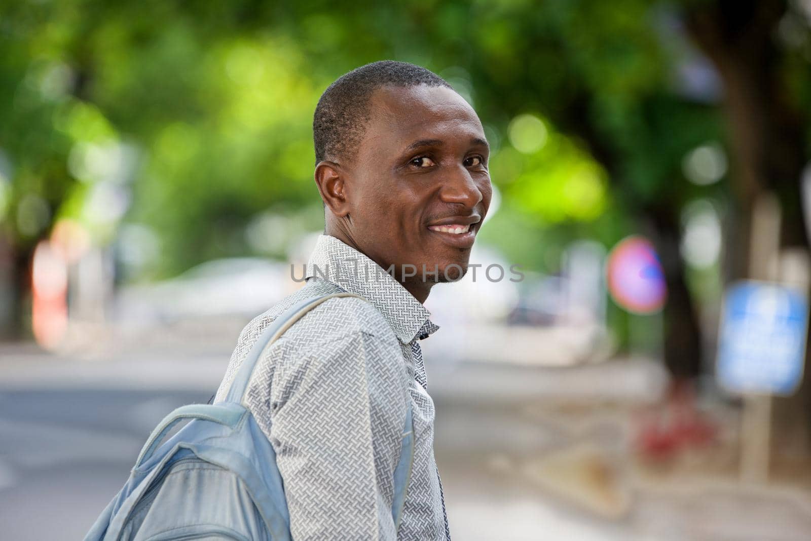 young man standing with backpack looking at the camera smiling.