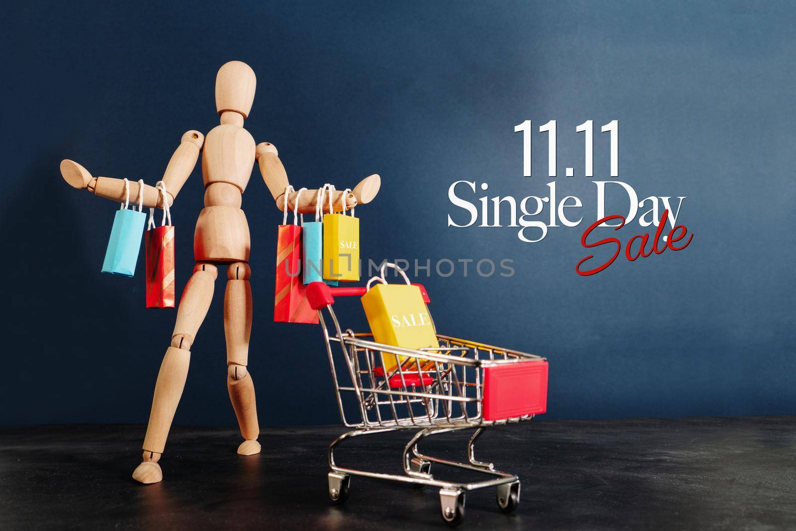 11.11 singles day sale concept, shopaholic wooden doll with lots of shopping bags on arm and shopping cart