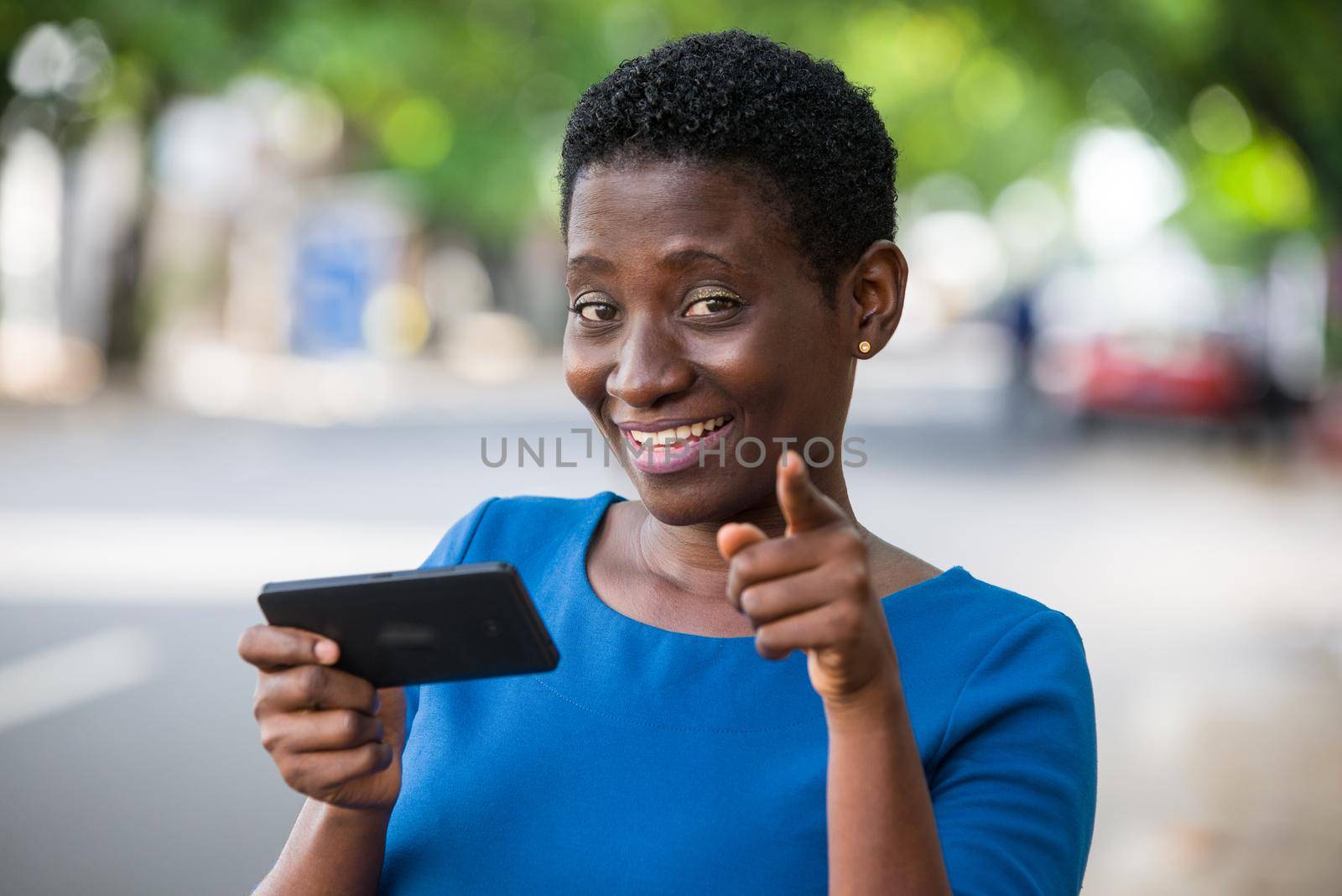 young girl standing in blue camisole cellphone in hand watching the camera smiling.