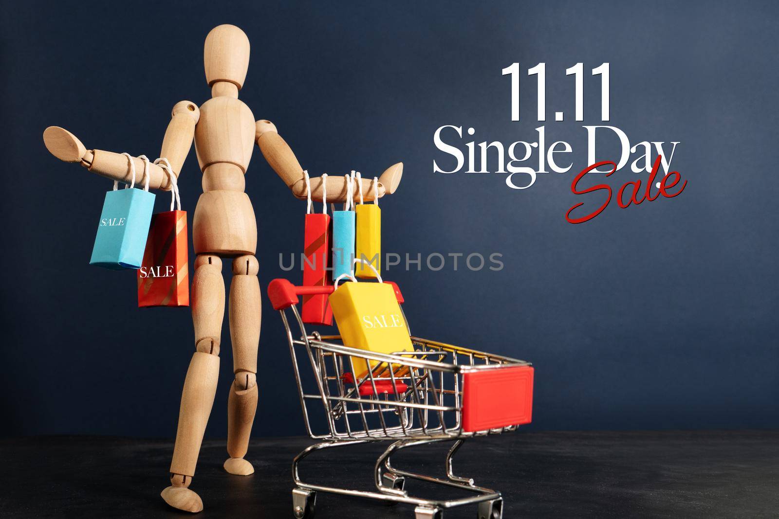 11.11 singles day sale concept, shopaholic wooden doll with lots of shopping bags on arm and shopping cart