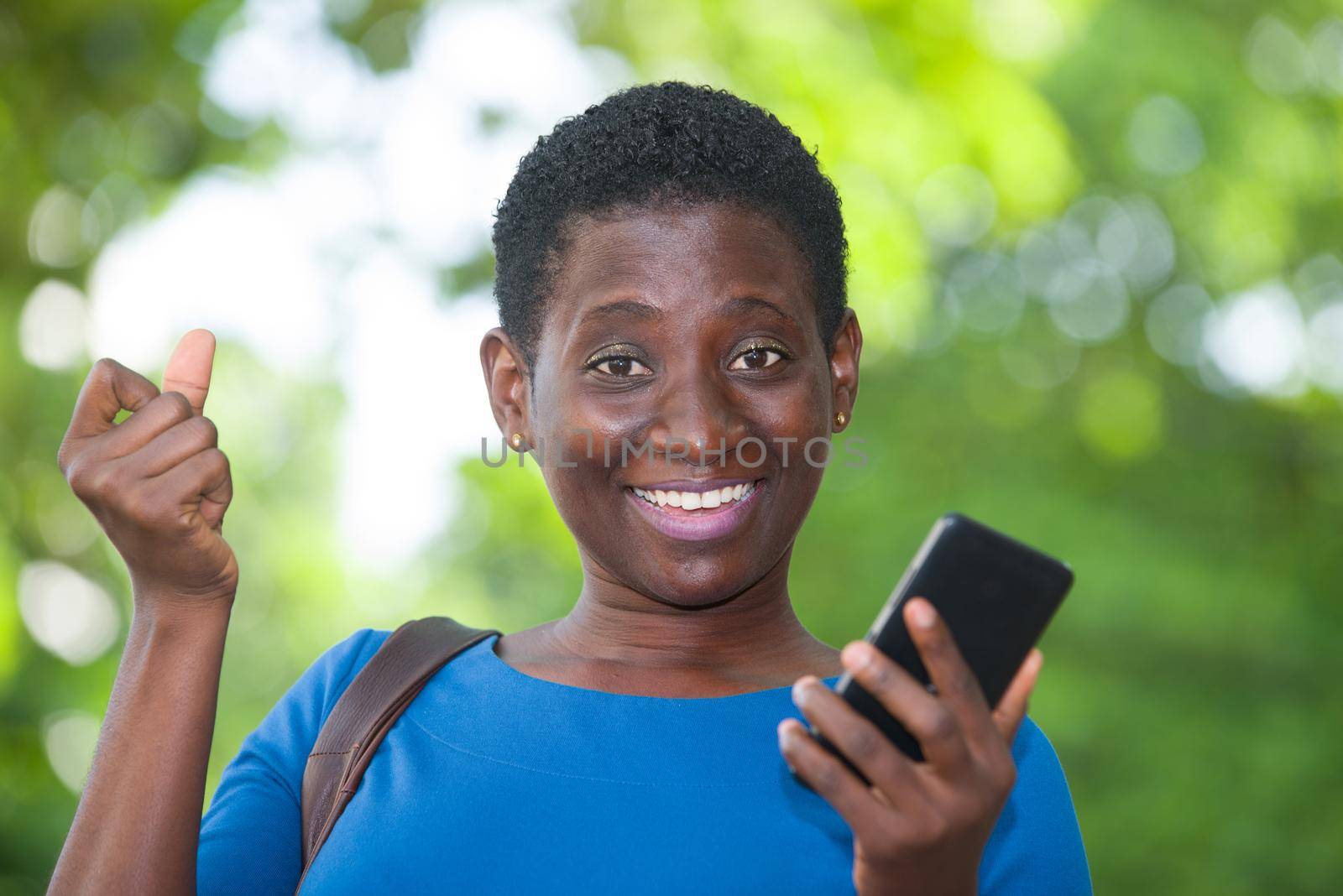 young girl standing in blue camisole cellphone in hand watching the camera smiling.