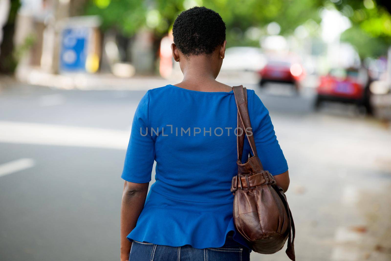 young girl in blue camisole with handbag walking while giving back to the camera.
