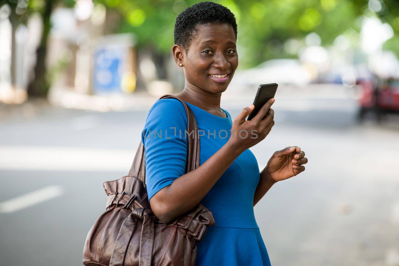 young girl standing in blue camisole with mobile phone looks at camera smiling.