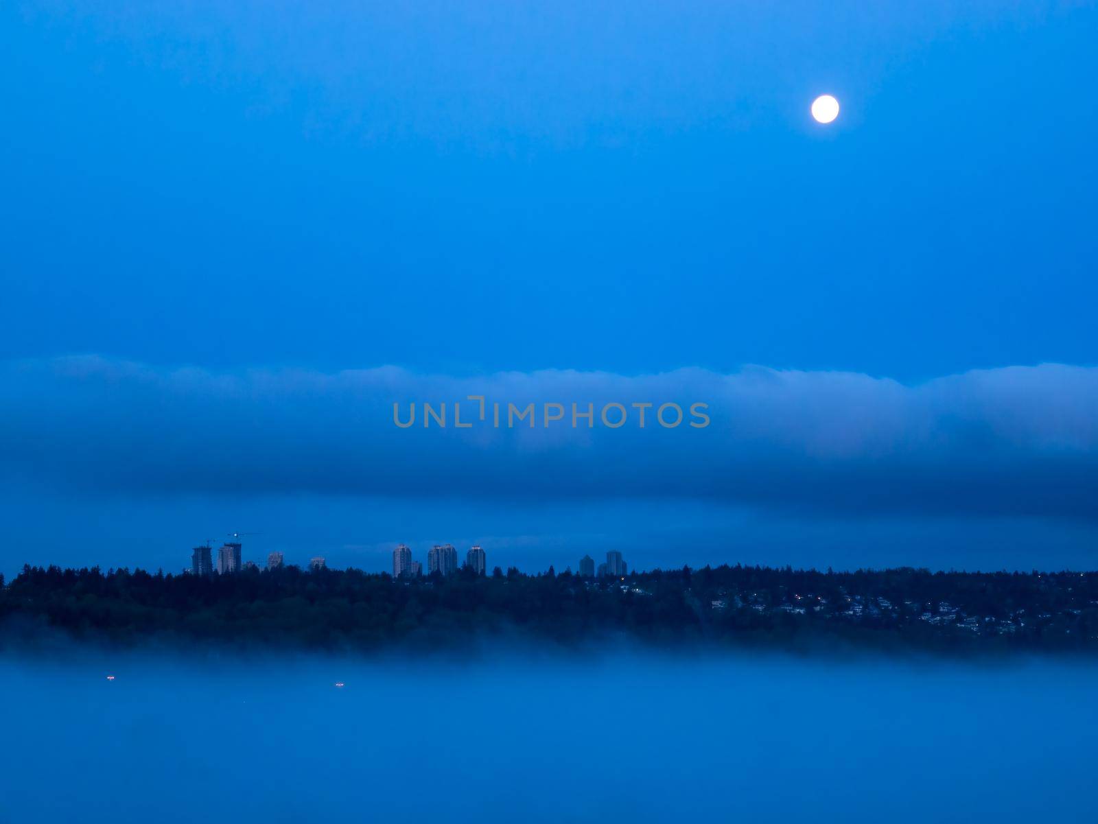 Night city in clouds with full moon over in the sky.