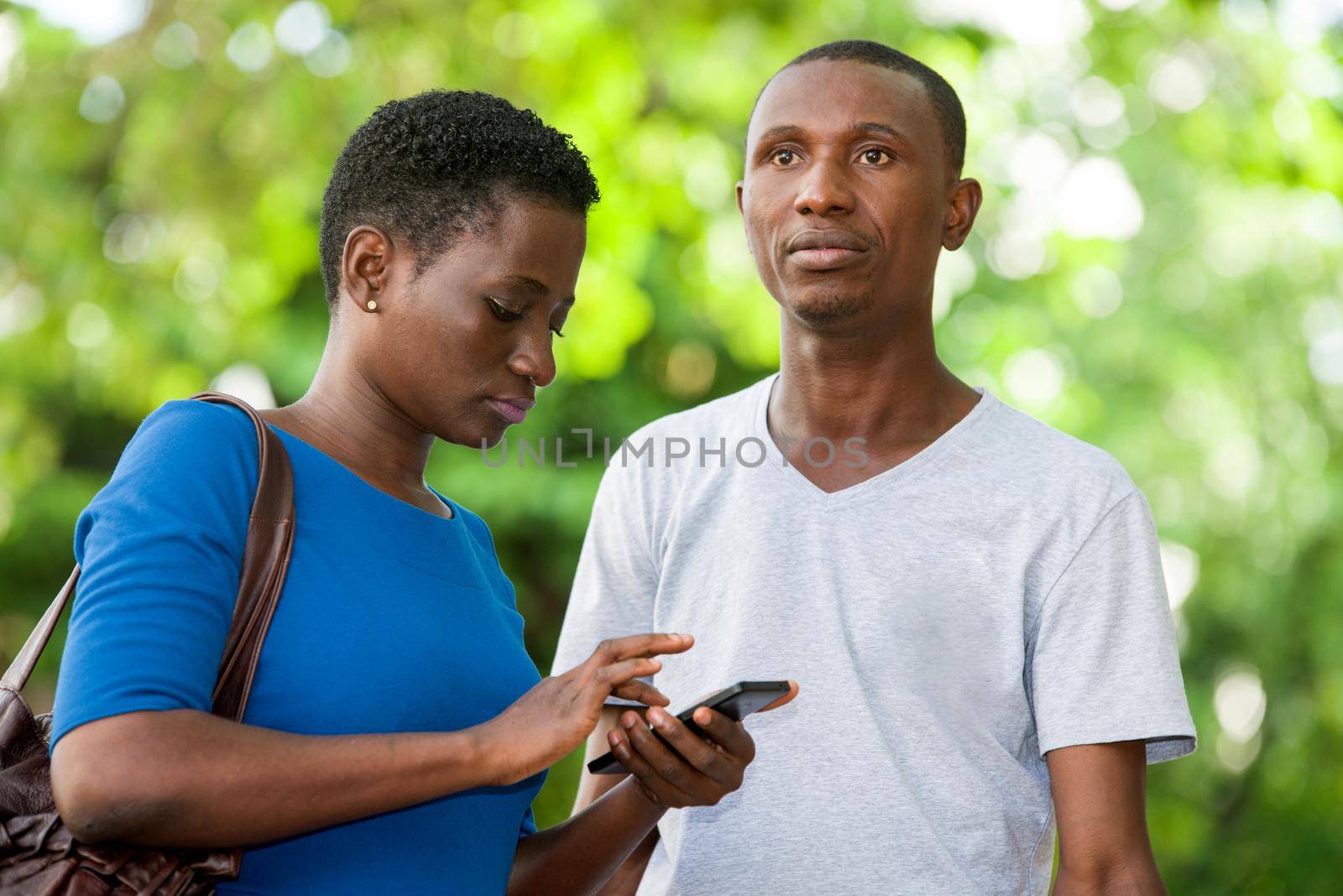 young girl standing in blue camisole looking at her cell phone while her friend looks in front of him with strange air.
