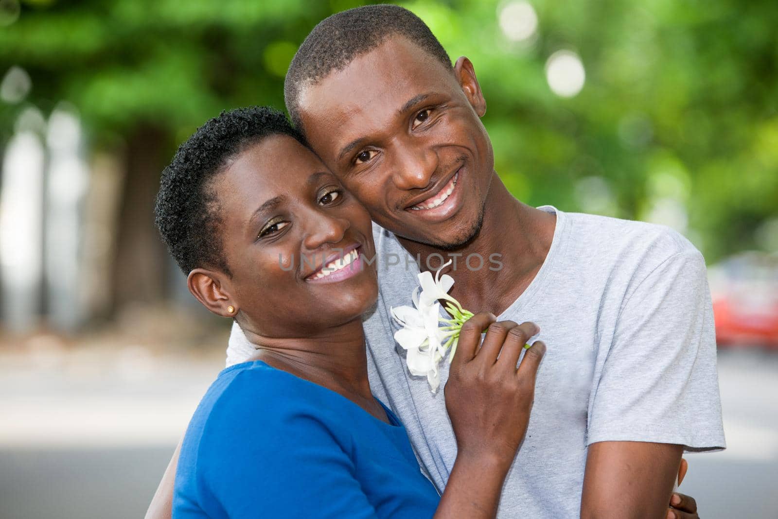 young couple standing with flower in hand embraced look at camera laughing.