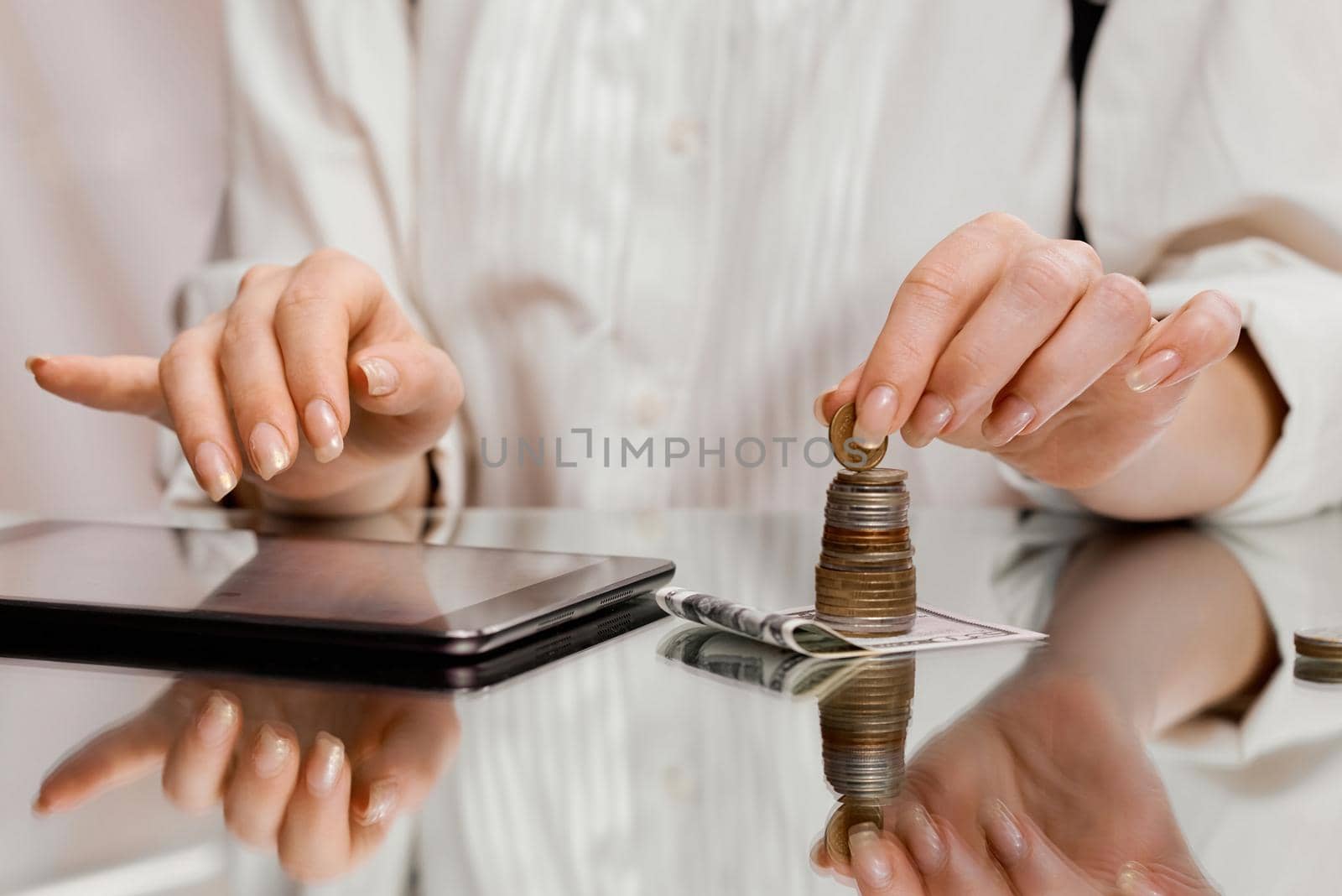 A woman counts finances on a tablet holding a coin from a stack on a banknote . High quality photo