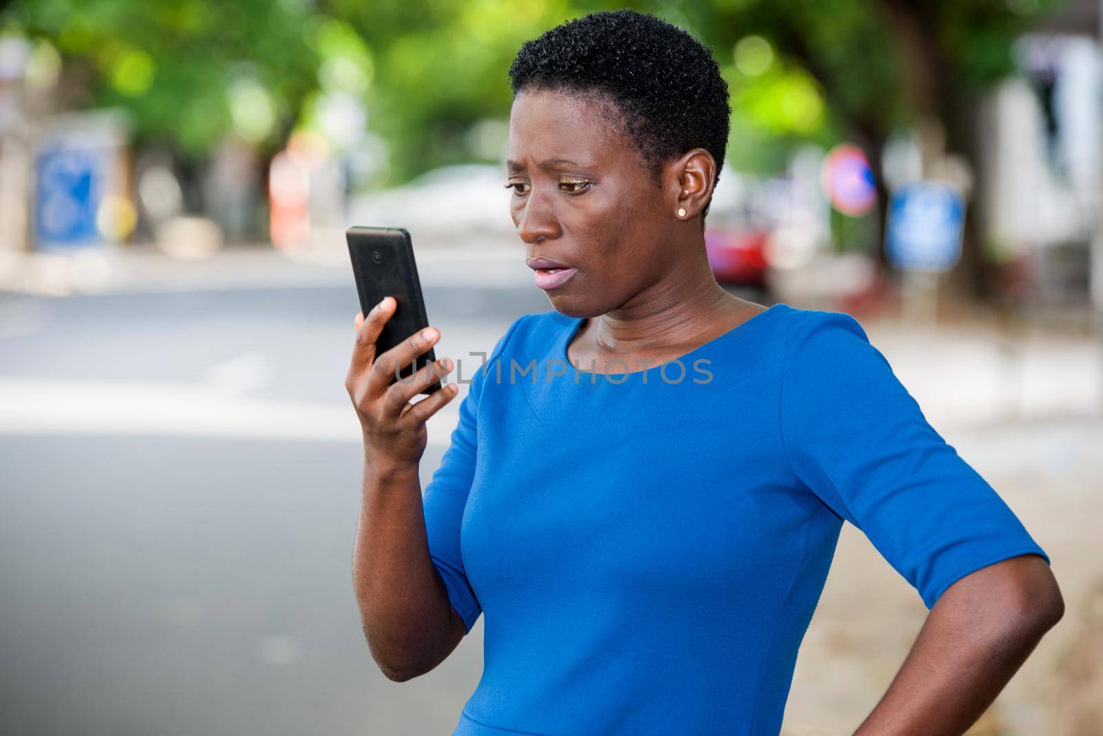 young girl standing in blue camisole looks at mobile phone with surprised look.