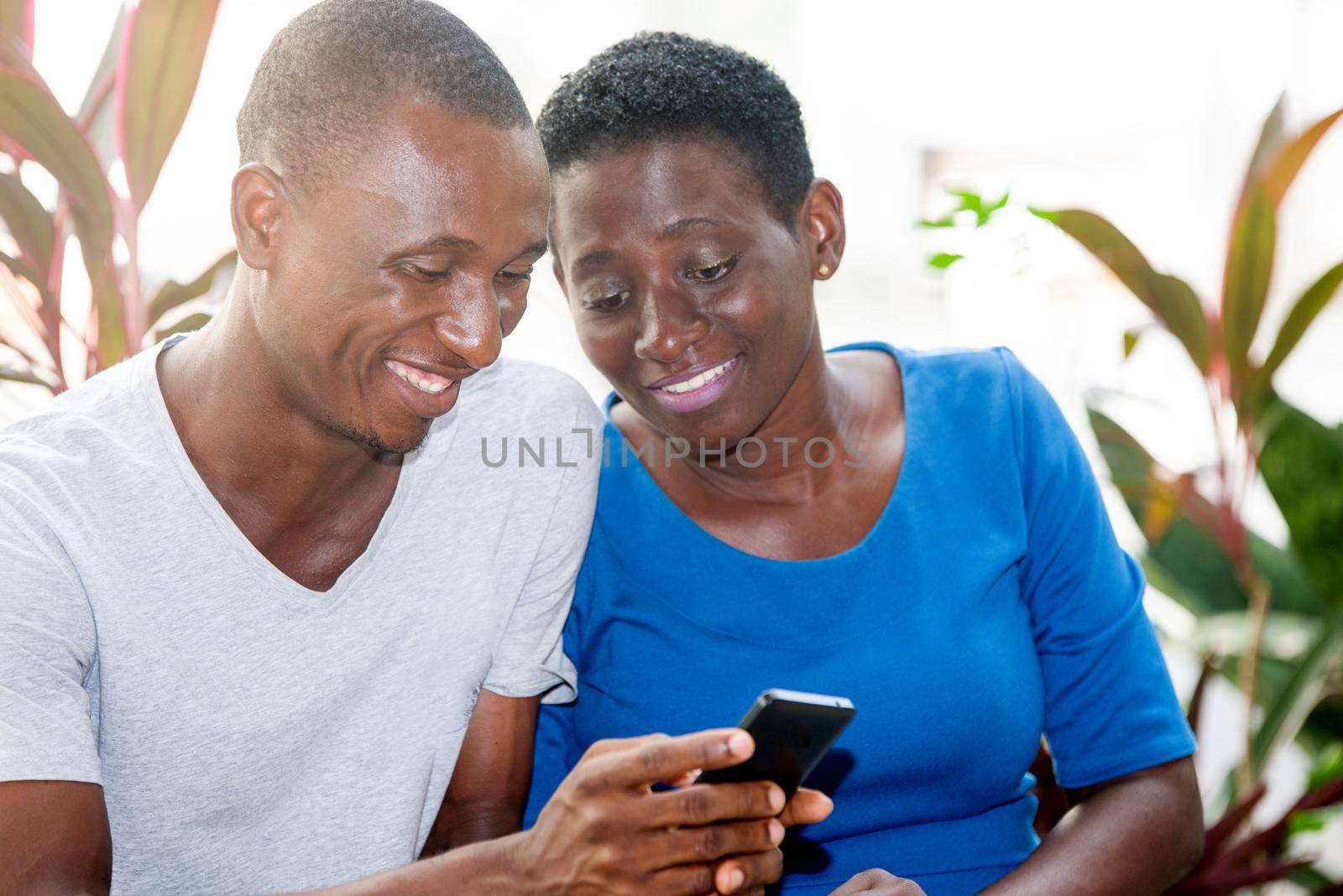 Young people sitting side by side in park cheer watching mobile phone while smiling.