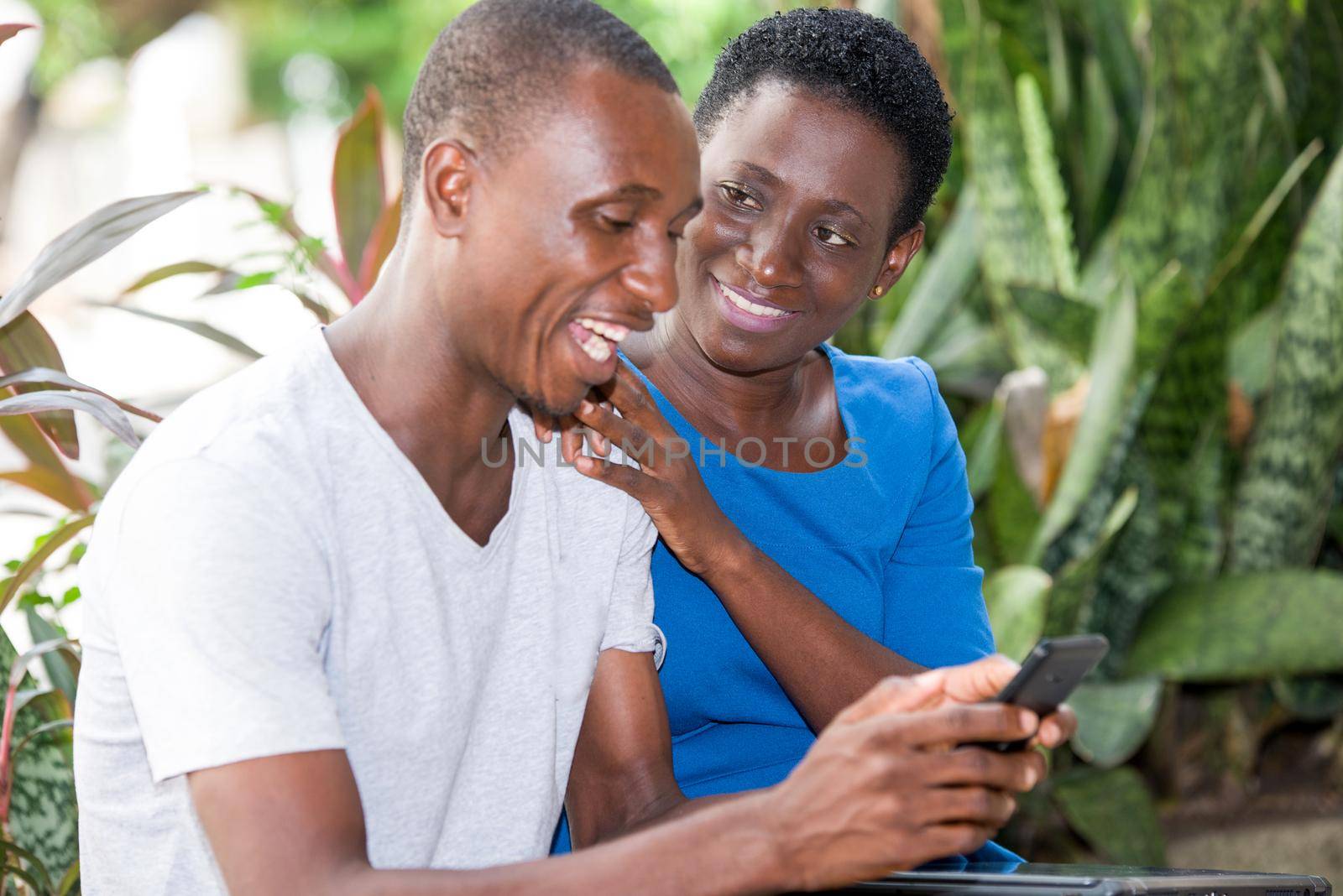 young couple sitting in park and look at mobile phone while smiling.