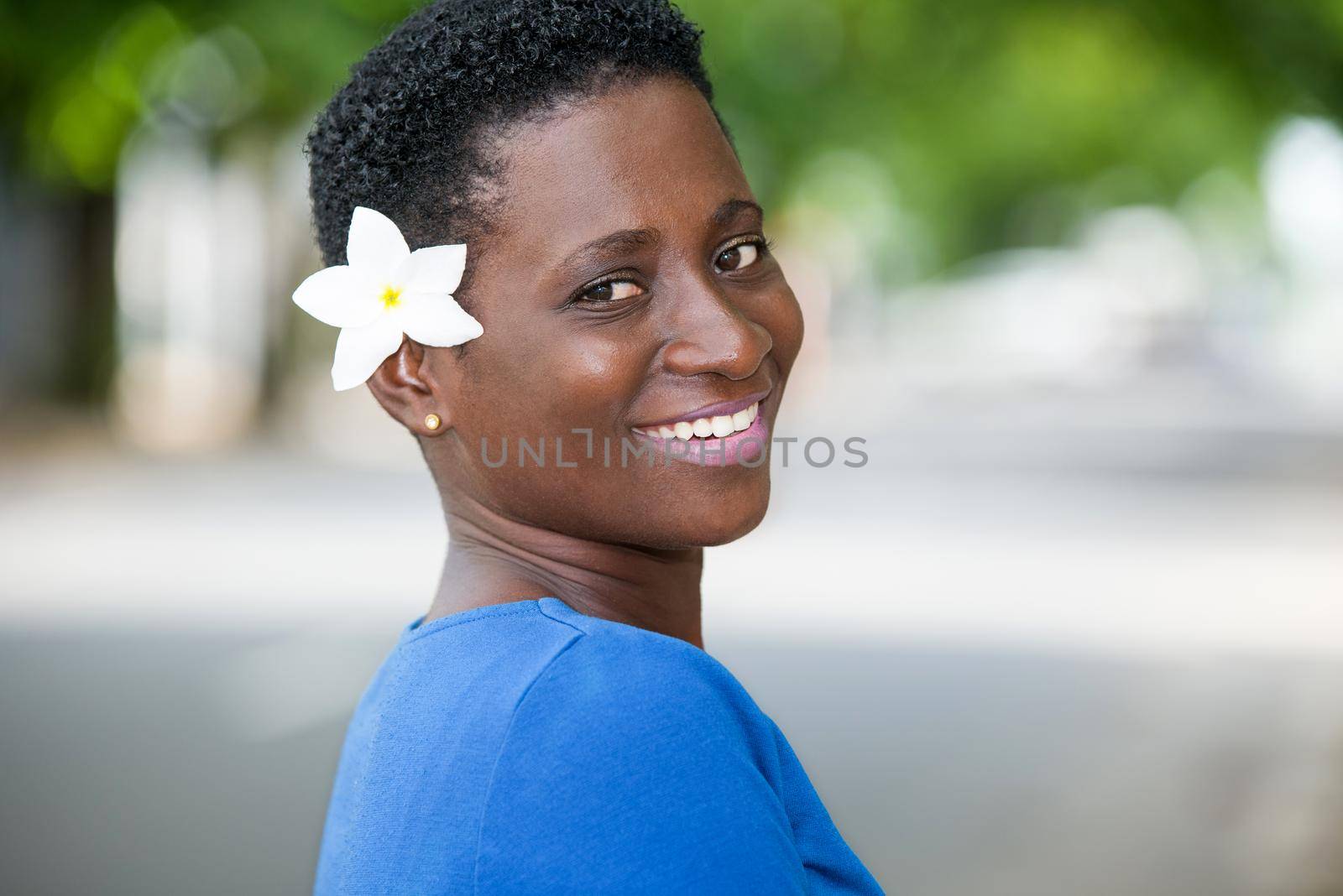 close-up of a happy young woman smiling outside and wearing a white flower on the ear