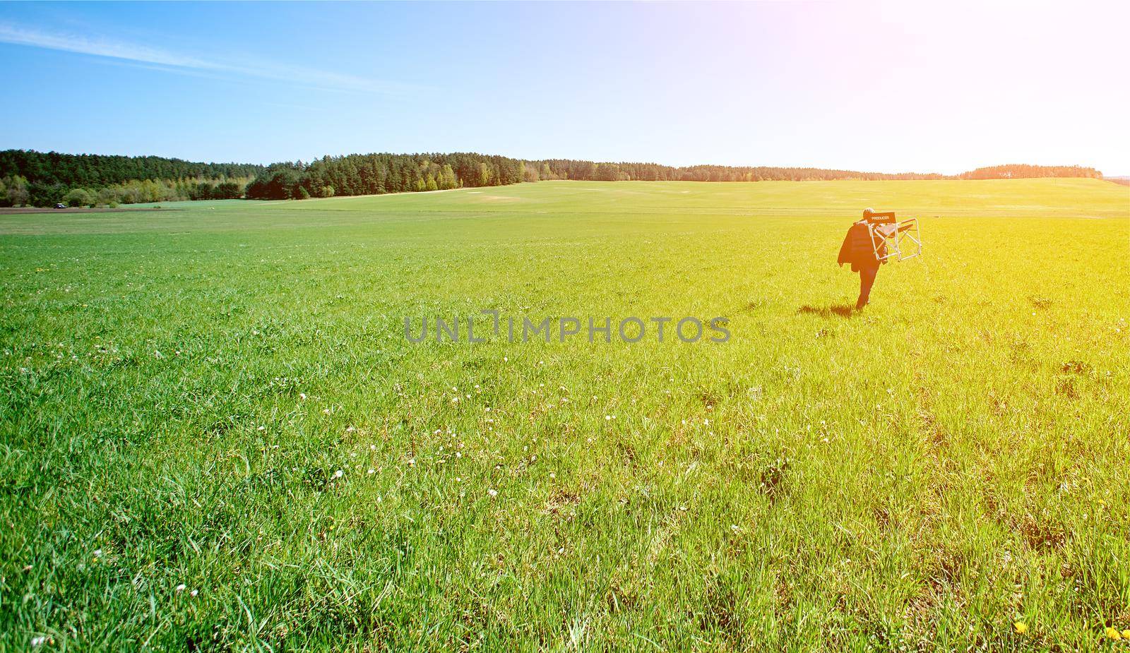 promiscuous man with a chair on his shoulder goes into the distance on the boundless green field by AntonIlchanka