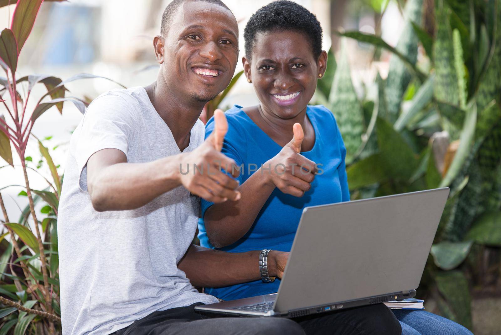 young students sitting in park with laptop wave fingers smiling on camera.