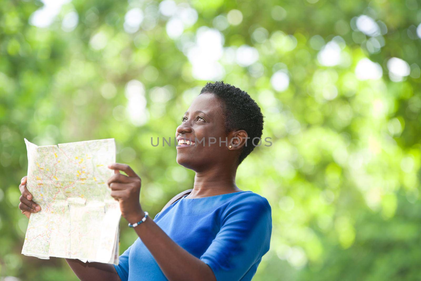 young woman standing in blue camisole with map in hand looking up laughing.