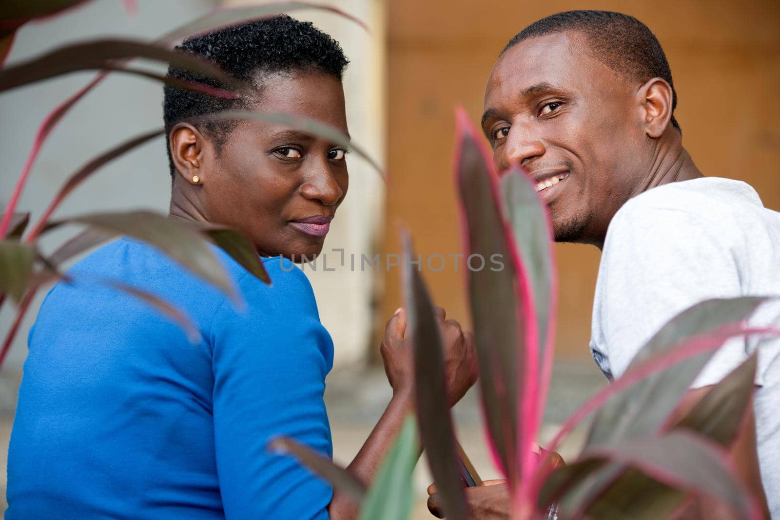 young couple sitting in park watching the camera smiling.