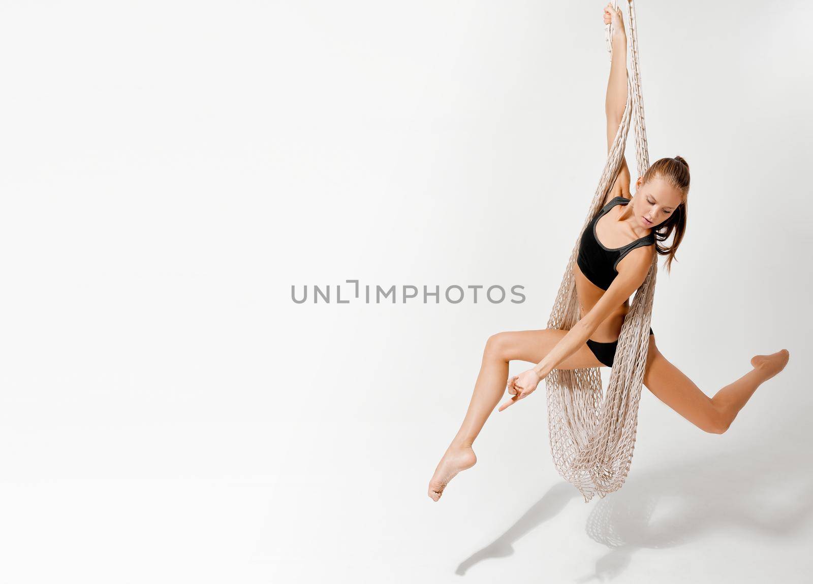 Girl acrobat gymnast hangs on a mesh against a white background. High quality photo