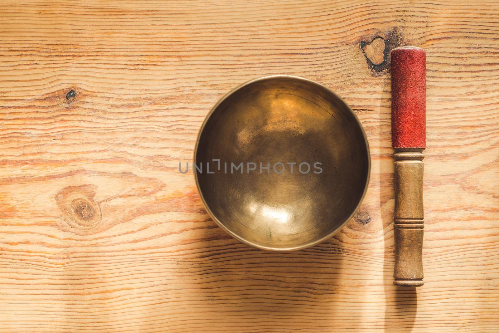 Tibetan copper bowl and wooden stick on wooden table with copy space.