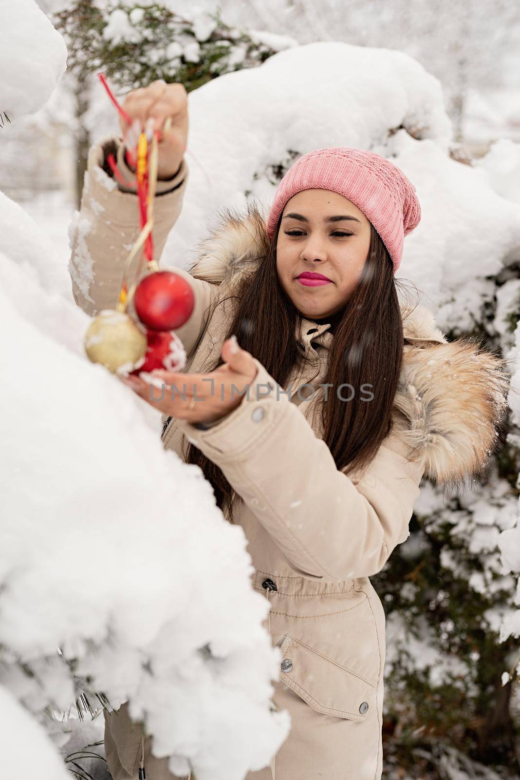 Merry Christmas and happy New Year. Beautiful woman in warm winter clothes decorating Christmas tree in a park in snowy day