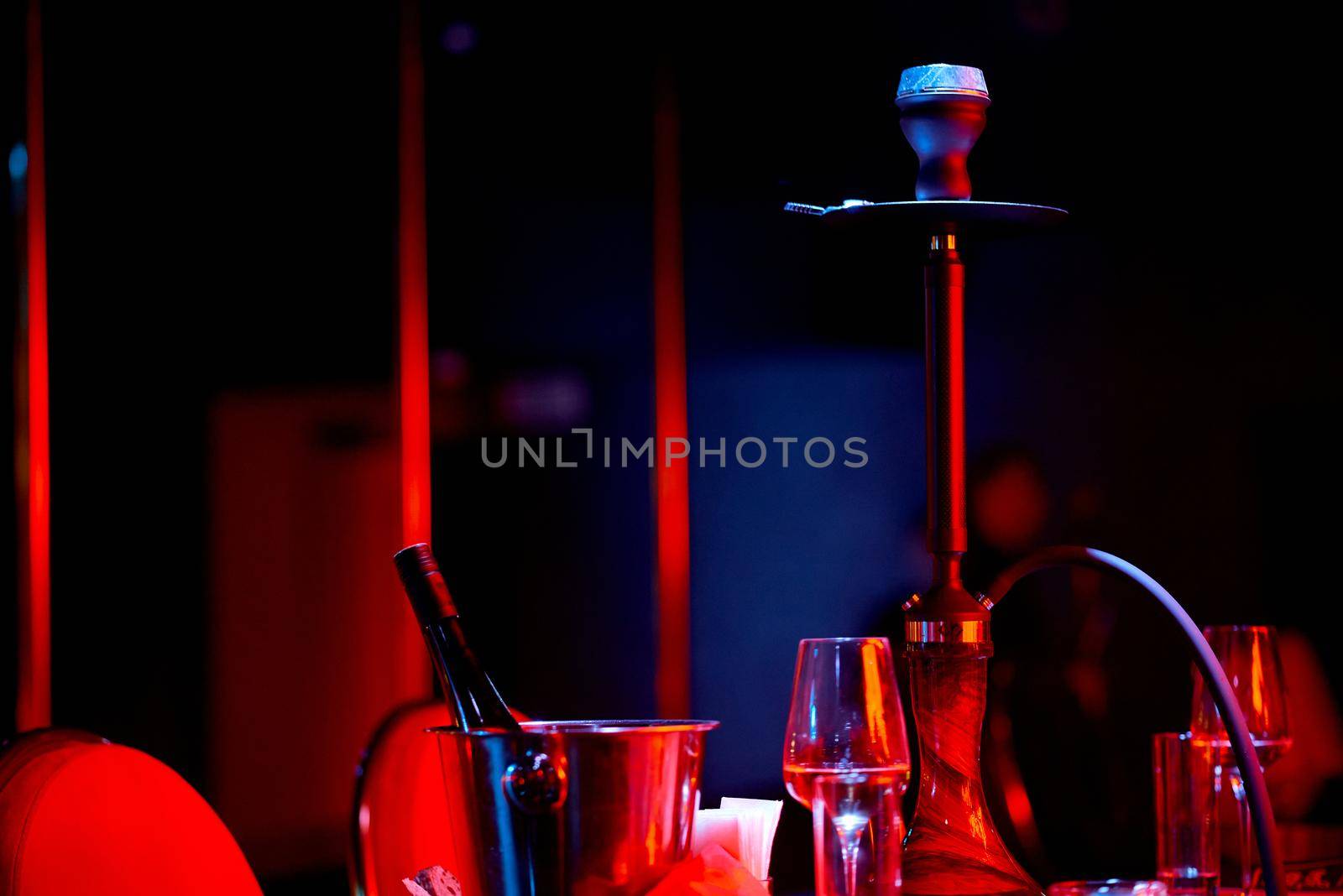 classic hookah on the table in blue and red light with glasses and a bucket with wine. High quality photo