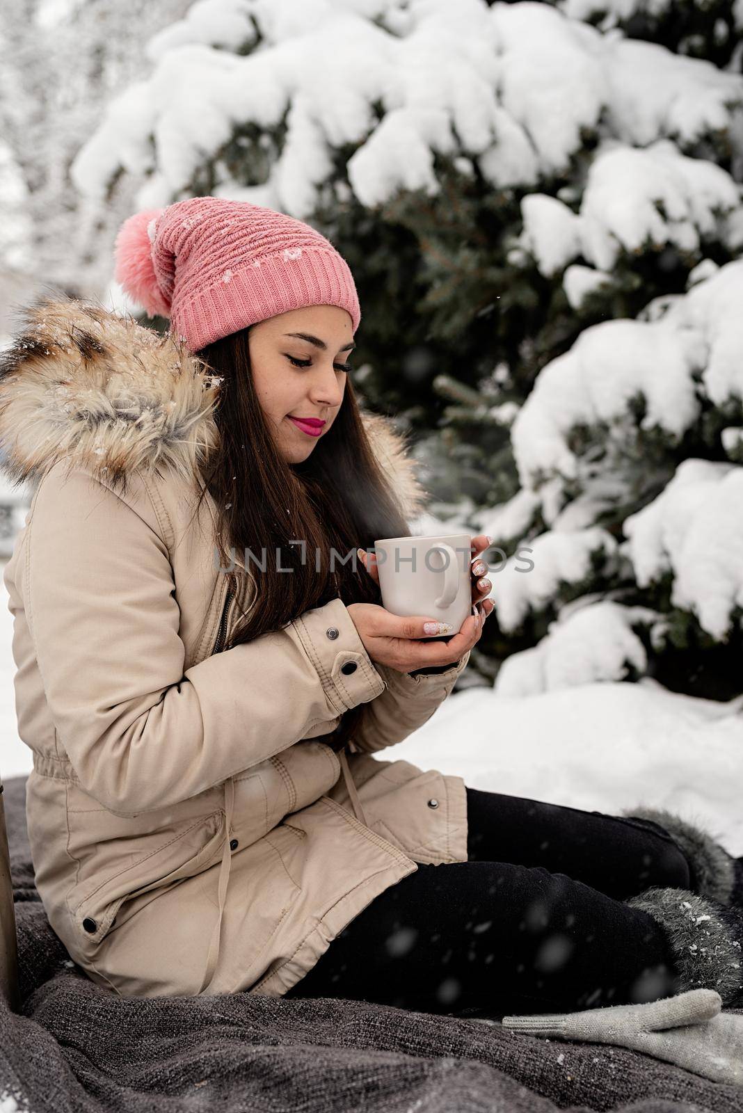 Beautiful woman in warm winter clothes holding cup drinking hot tea or coffee outdoors in snowy day by Desperada