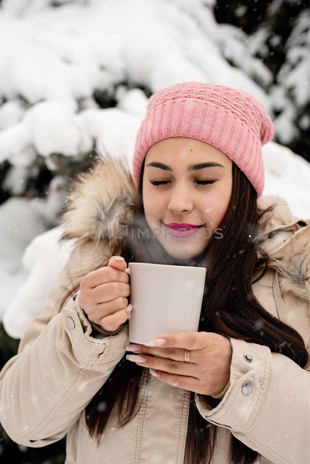 Merry Christmas and happy New Year. Beautiful woman in warm winter clothes holding mug drinking hot tea or coffee outdoors in snowy day