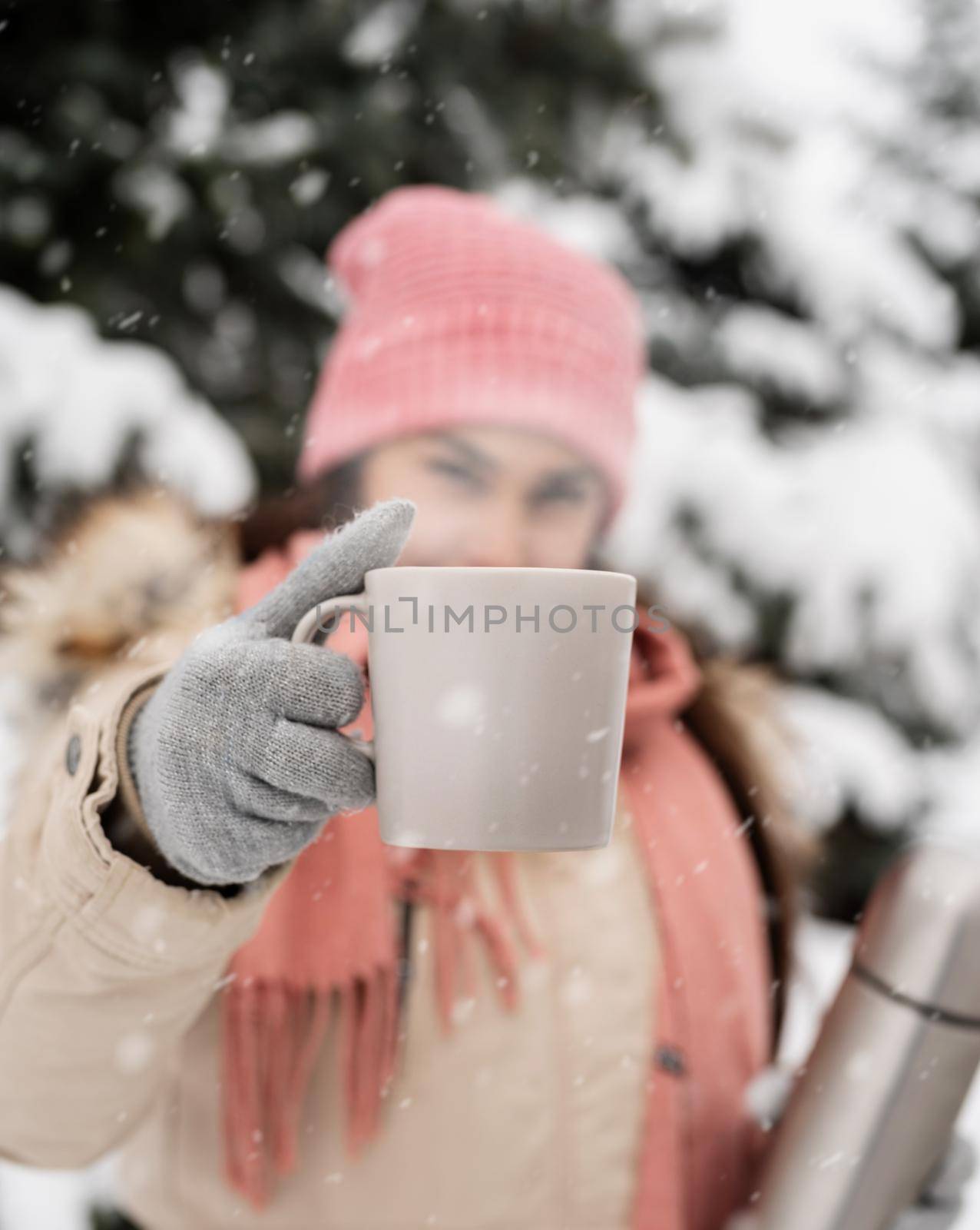 Merry Christmas and happy New Year. Beautiful woman in warm winter clothes holding thermos and drinking hot tea or coffee outdoors in snowy day