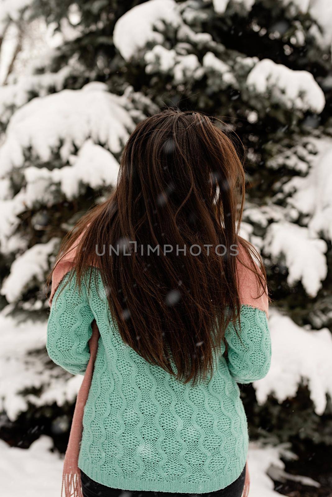 Back view of brunette woman in pink winter clothes standing outdoors in snowy day by christmas tree by Desperada