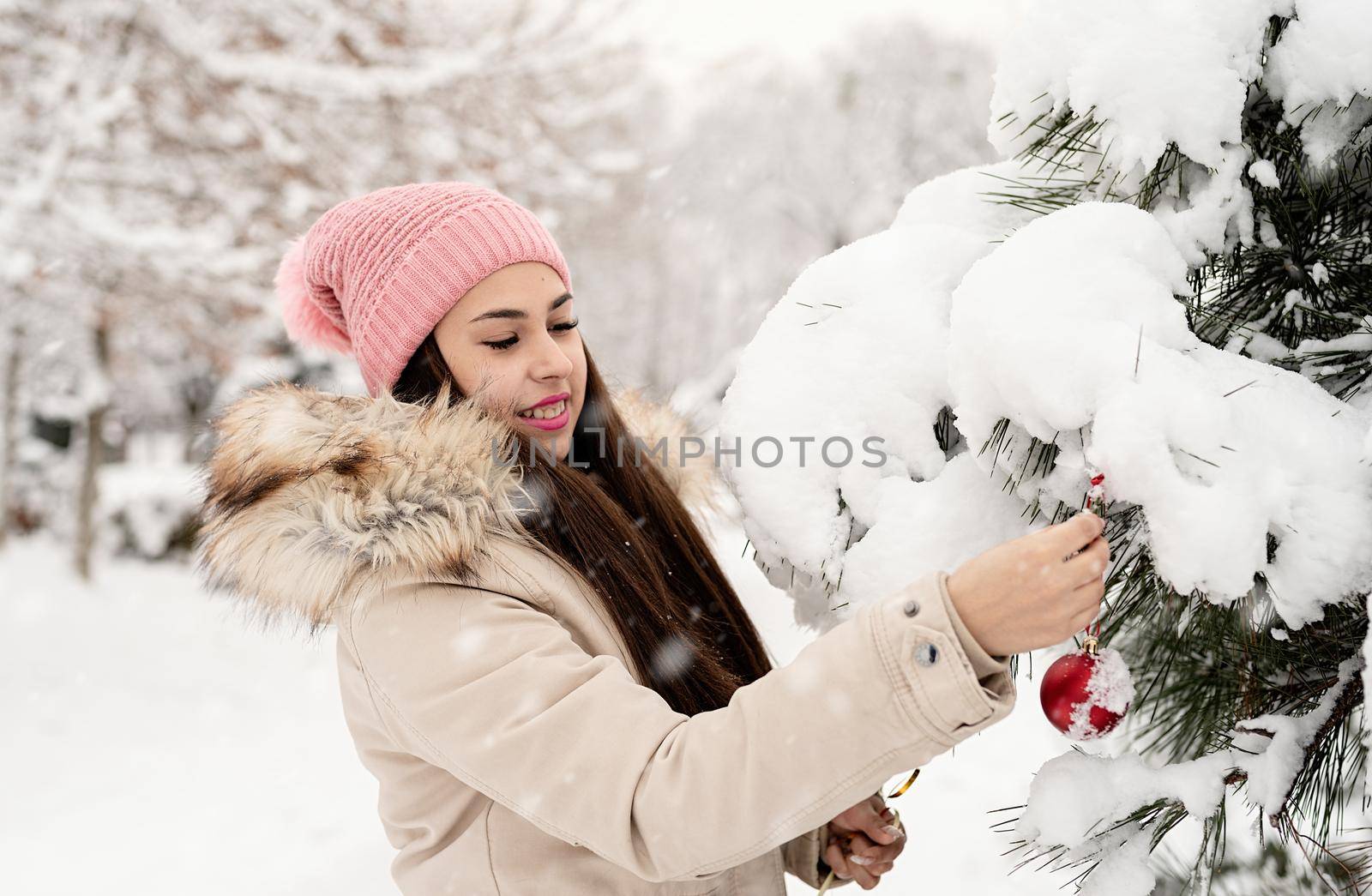 Merry Christmas and happy New Year. Beautiful woman in warm winter clothes decorating Christmas tree in a park in snowy day
