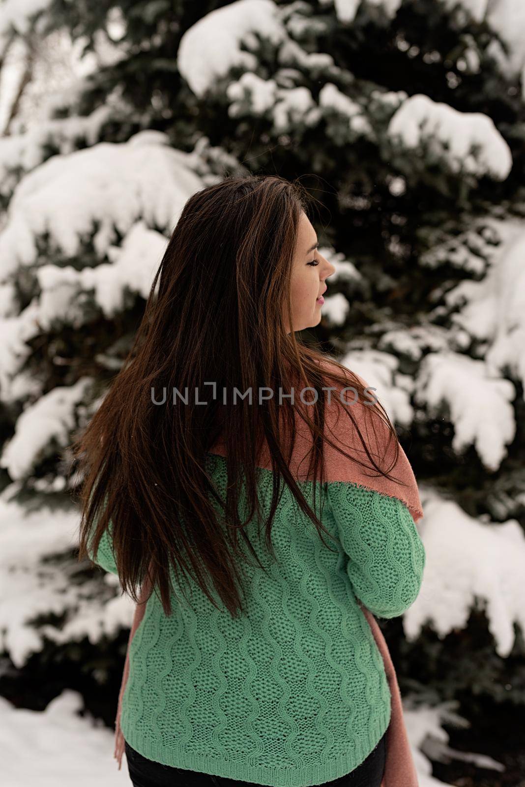 Back view of brunette woman in pink winter clothes standing outdoors in snowy day by christmas tree by Desperada