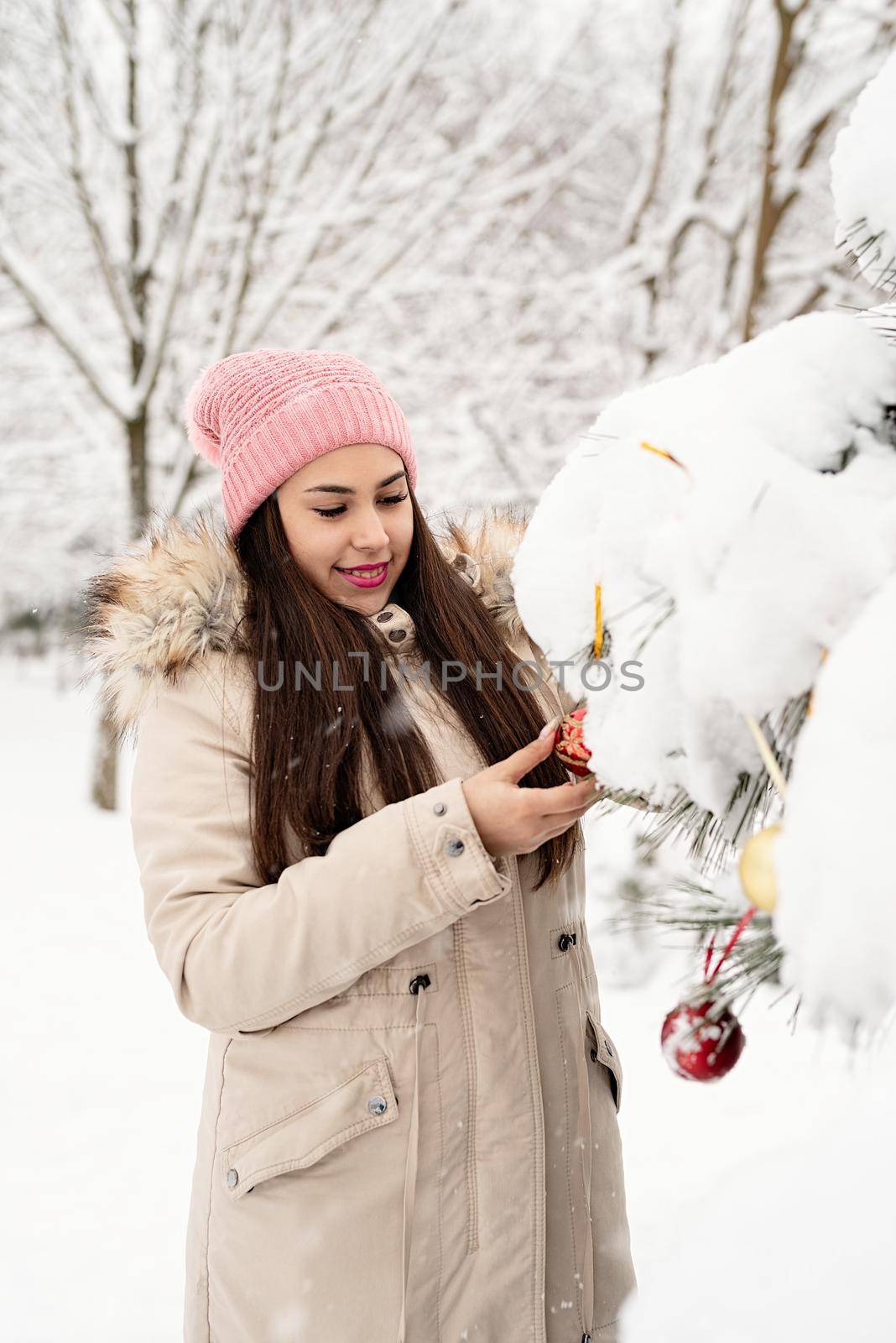 Merry Christmas and happy New Year. Beautiful woman in warm winter clothes decorating Christmas tree in a park in snowy day