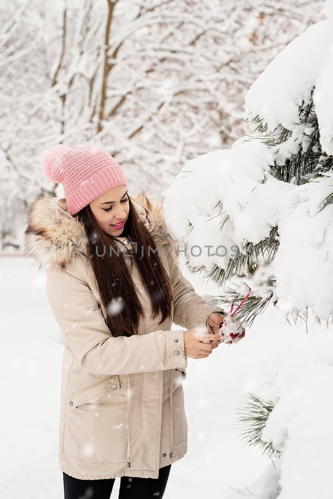Beautiful woman in warm winter clothes decorating Christmas tree in a park in snowy day by Desperada