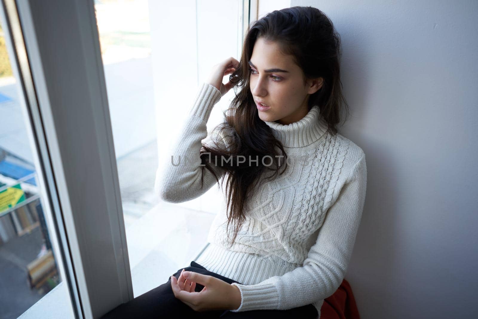 pretty woman in white sweater near the window alone. High quality photo