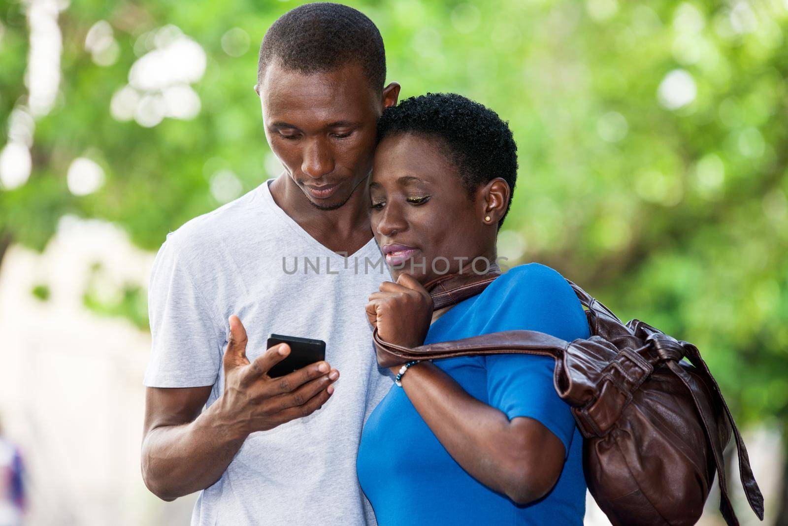 two students standing in park and look at mobile phone while smiling.